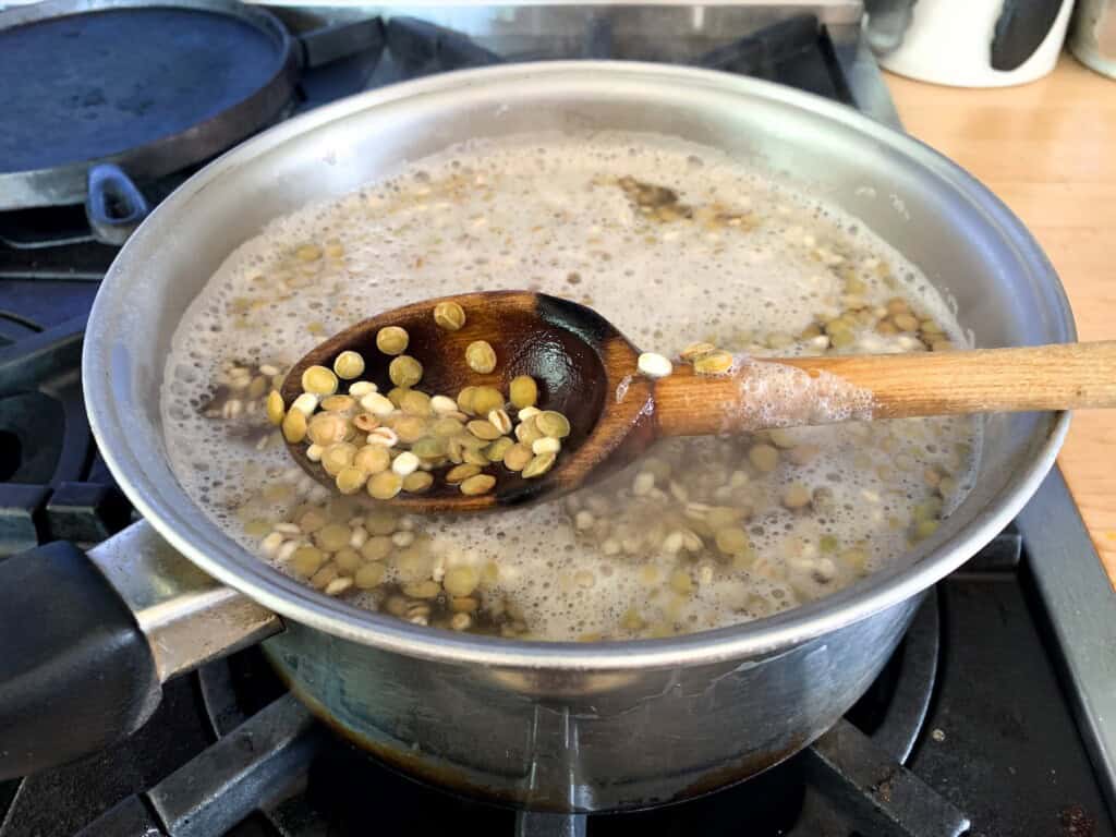 A saucepan of lentils and barley cooking in boiling water on the stove. 