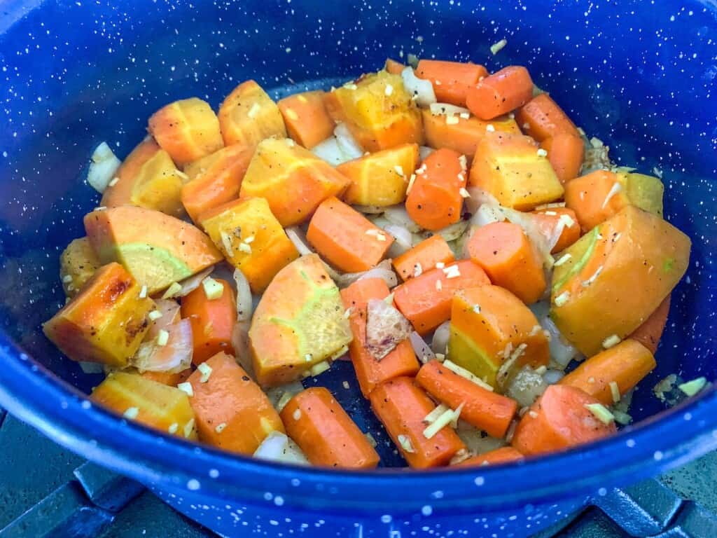 Carrots, onions, and ginger in a blue soup pot being sautéed. 