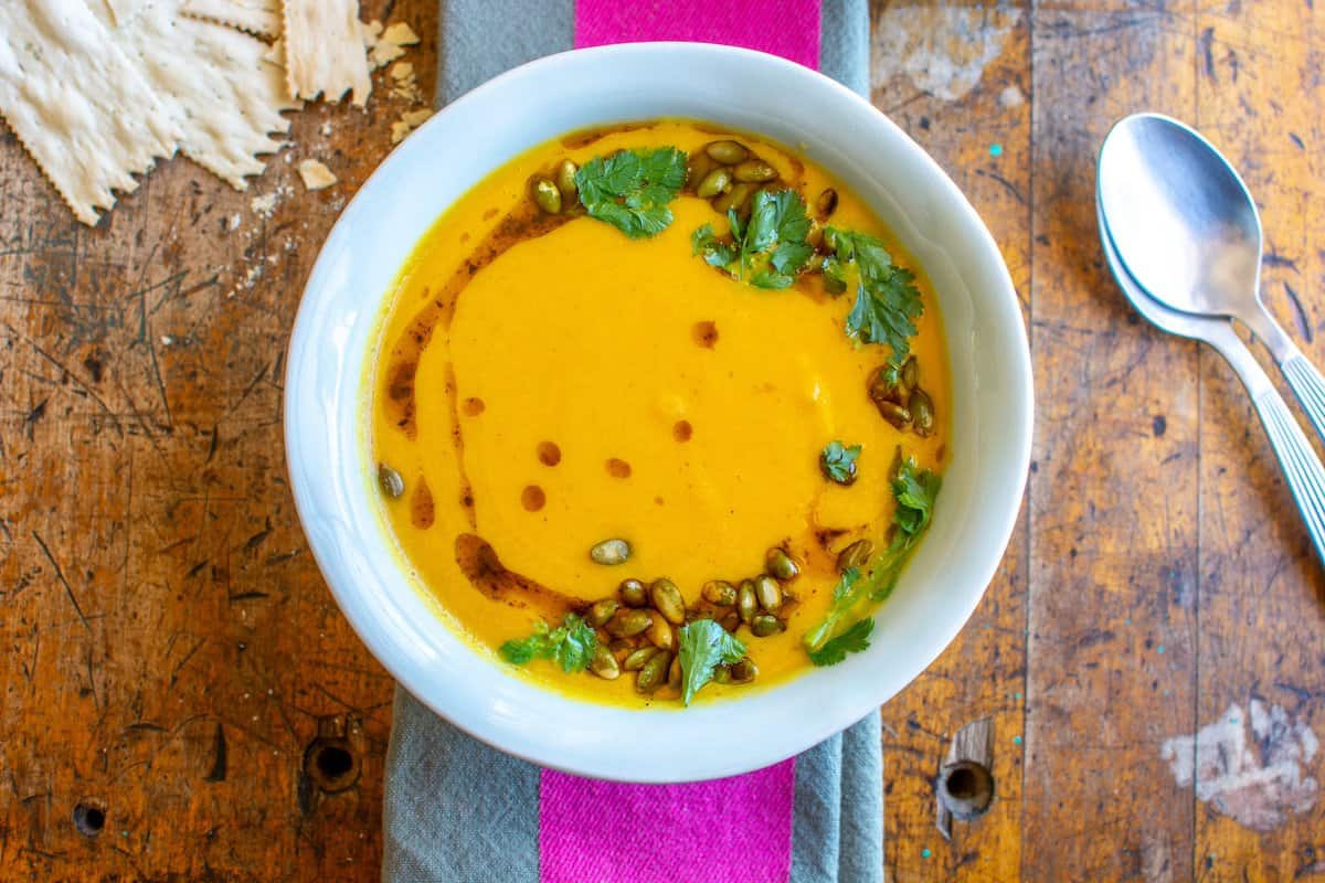 A bowl of butternut squash and carrot soup on a pink and grey kitchen towel.