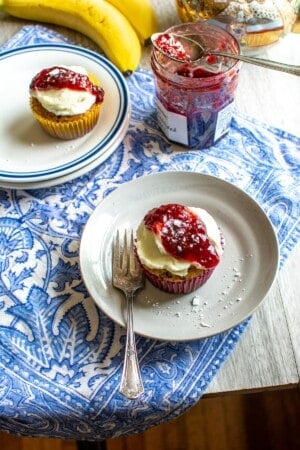 Two banana cupcakes topped with cream cheese frosting and raspberry jam.