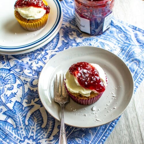 Two banana cupcakes topped with cream cheese frosting and raspberry jam.