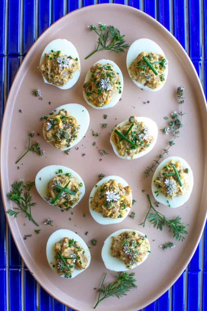 cajun shrimp deviled eggs on a pink platter on a blue tile table. 