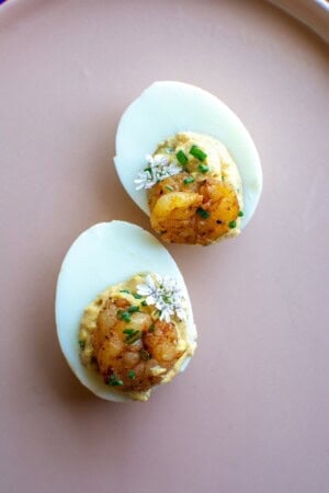 Two deviled eggs on a pink platter with baby shrimp on top.