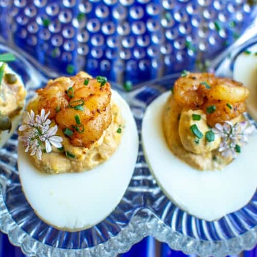 Two deviled eggs on a platter with baby shrimp on top.