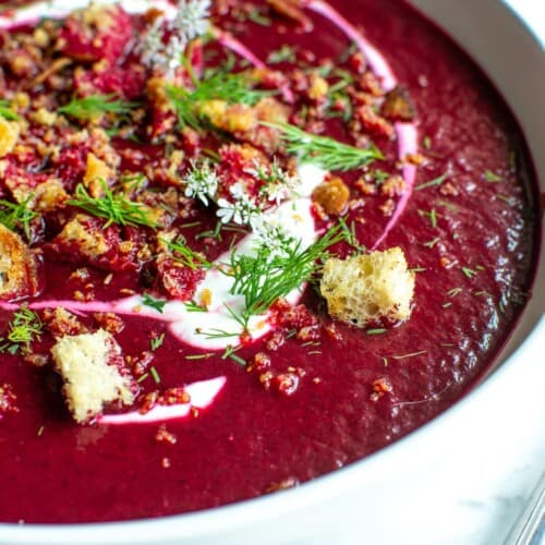 A white bowl filled with chilled beet borscht topped with croutons.