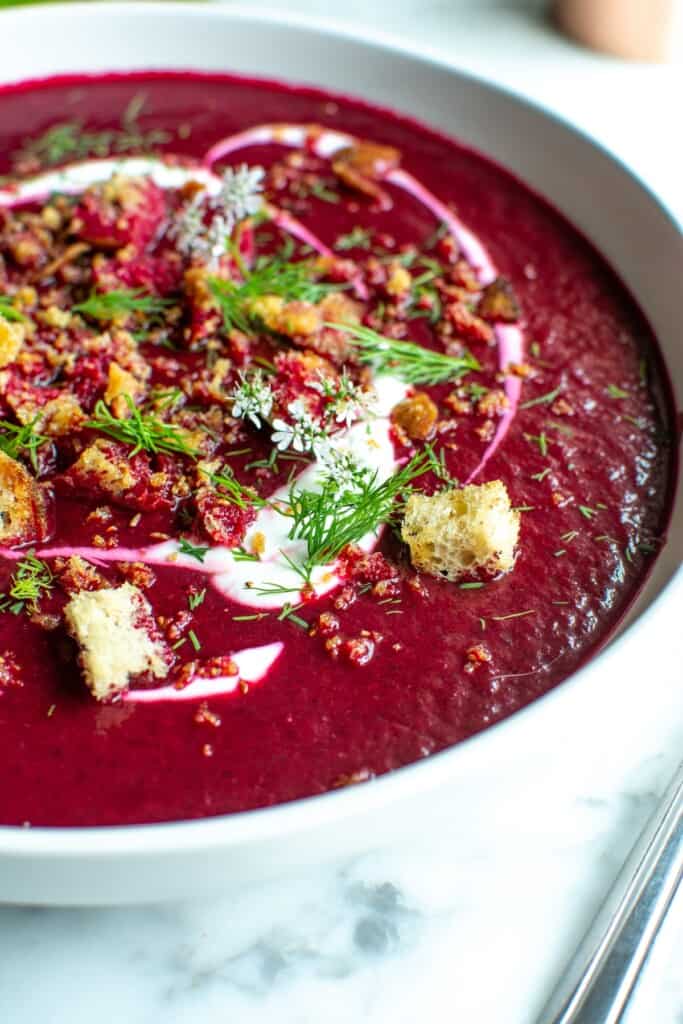 A white bowl filled with chilled beet borscht topped with croutons. 