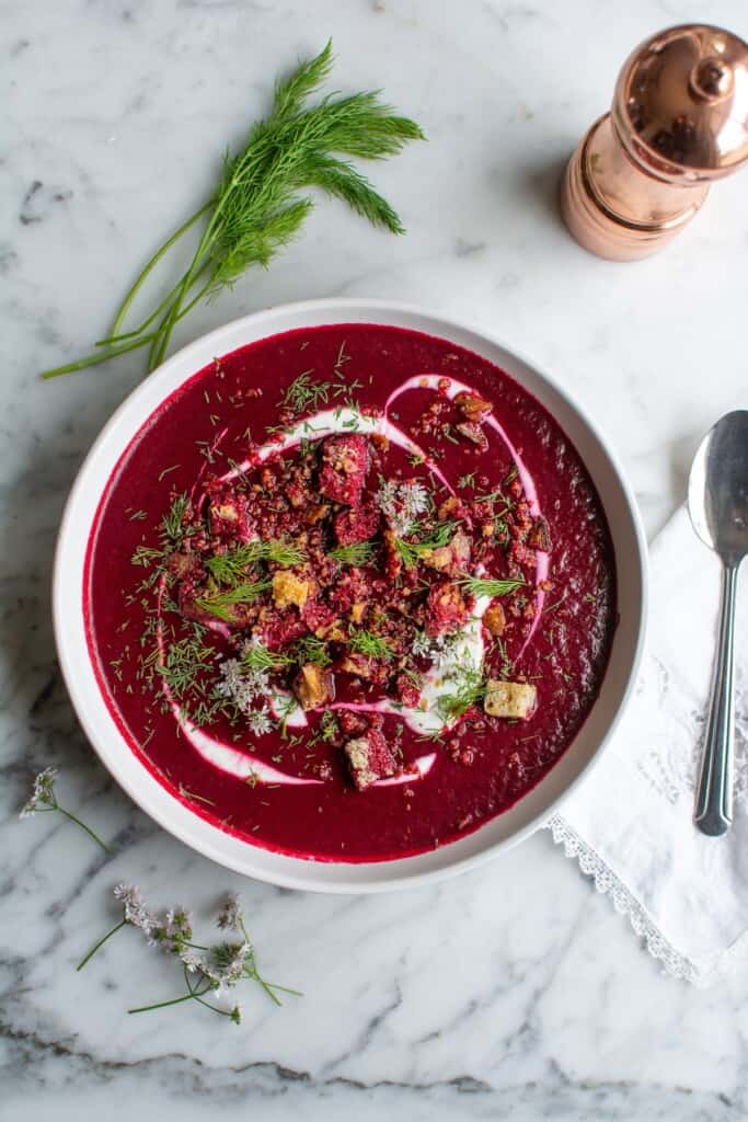 A white bowl filled with red beet borscht topped with sour cream. 