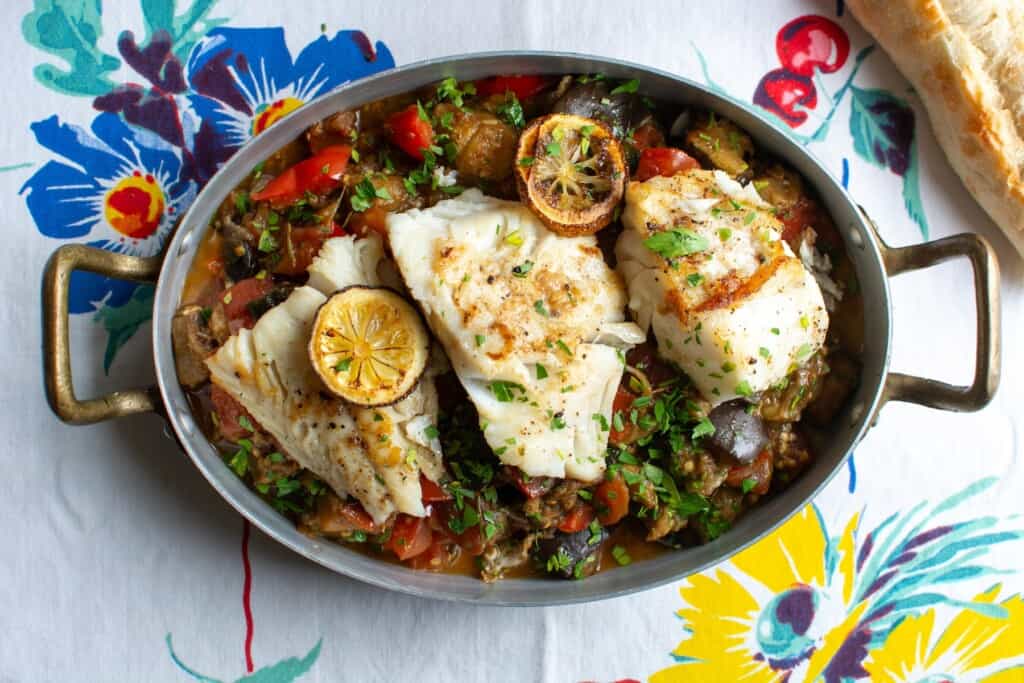 A copper dish full of Ratatouille with pieces of cod on top. 