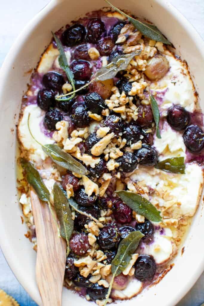 An overhead close up image of baked goat cheese dip with roasted grapes and walnuts. 