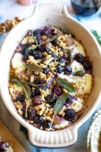 A dish of baked goat cheese with a wine glass in the background with red wine in it.