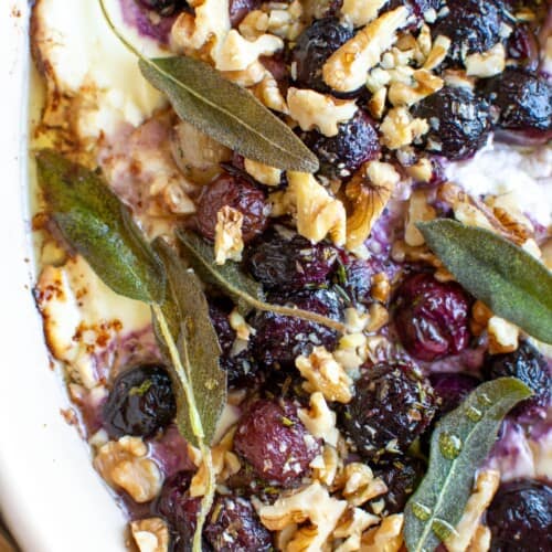 A close up of baked goat cheese dip topped with roasted grapes and walnuts.