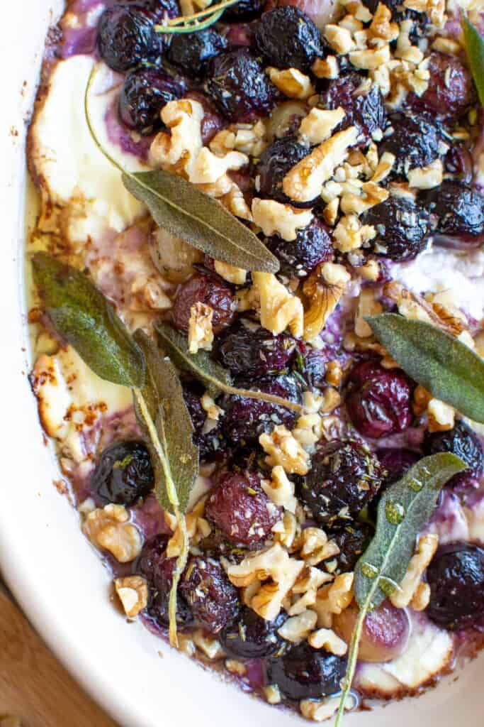 A close up of baked goat cheese dip topped with roasted grapes and walnuts. 