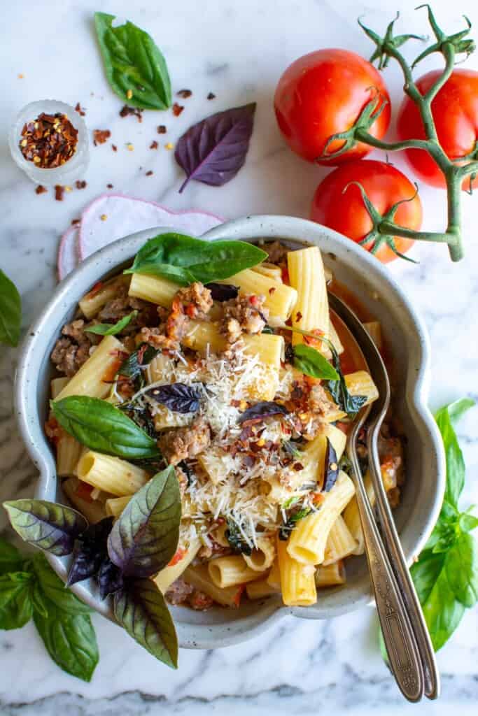 A bowl filled with rigatoni pasta with sausage and tomatoes. 