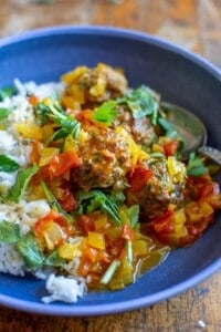 A blue bowl filled with white rice and pork meatballs in a tomato saffron sauce.