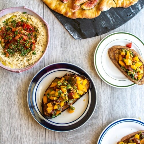 Several appetizers on a table including pizza, bruschetta, and hummus.