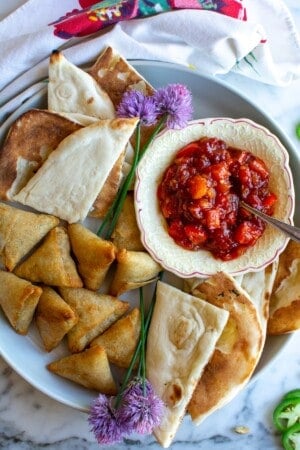 A plate of samosas with a bowl of tomato chutney on the plate.