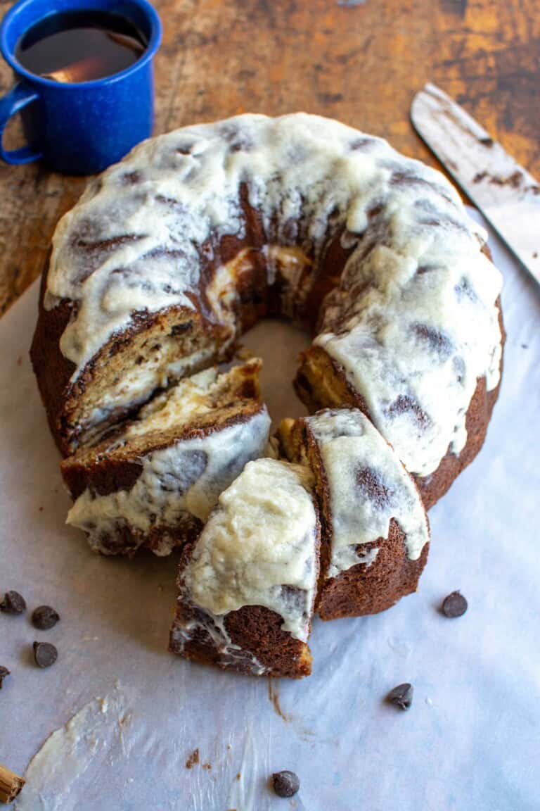 A banana bundt cake on a piece of white parchment paper next to a blue cup