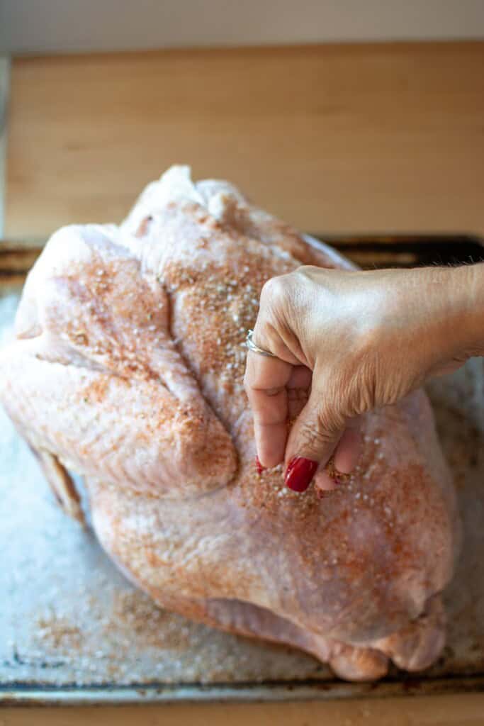 A hand sprinkling spice rub onto a turkey. 