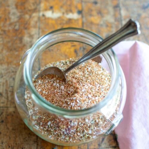 A jar of spice rub with a spoon in it and a pink napkin next to it.