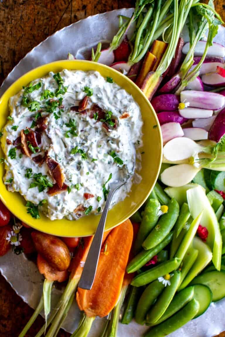 A close up of blue cheese dip in a yellow bowl with carrots around it.