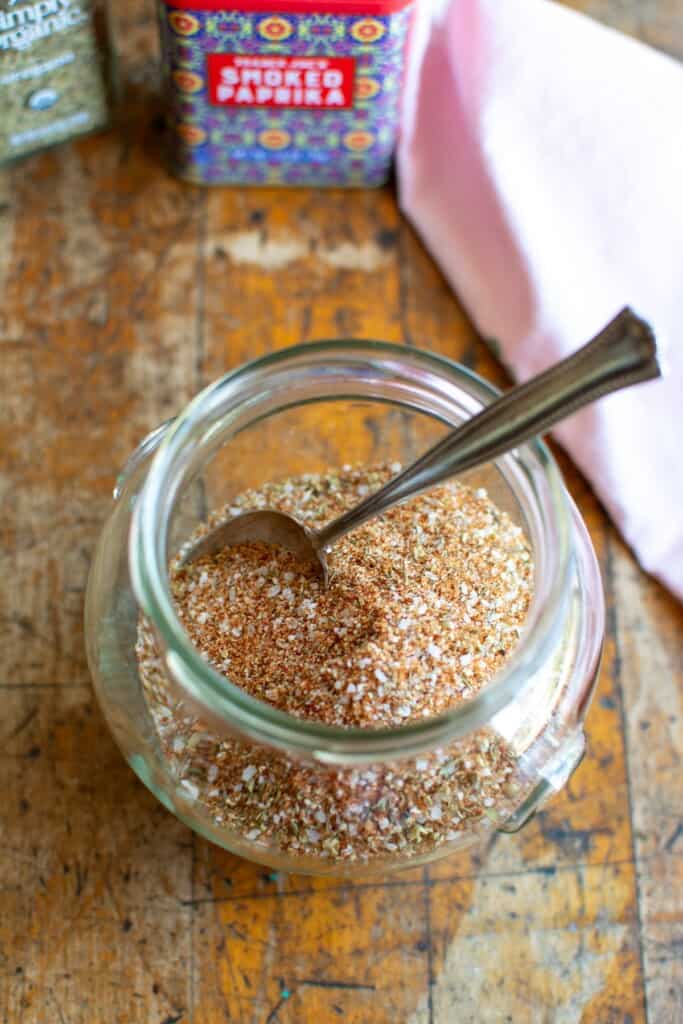 A jar of spice rub with a spoon in the jar and a pink napkin. 