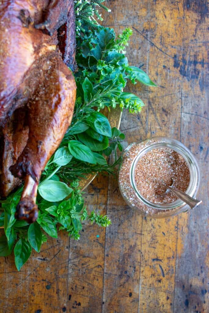 A jar of spice rub next to a smoked turkey on a platter. 