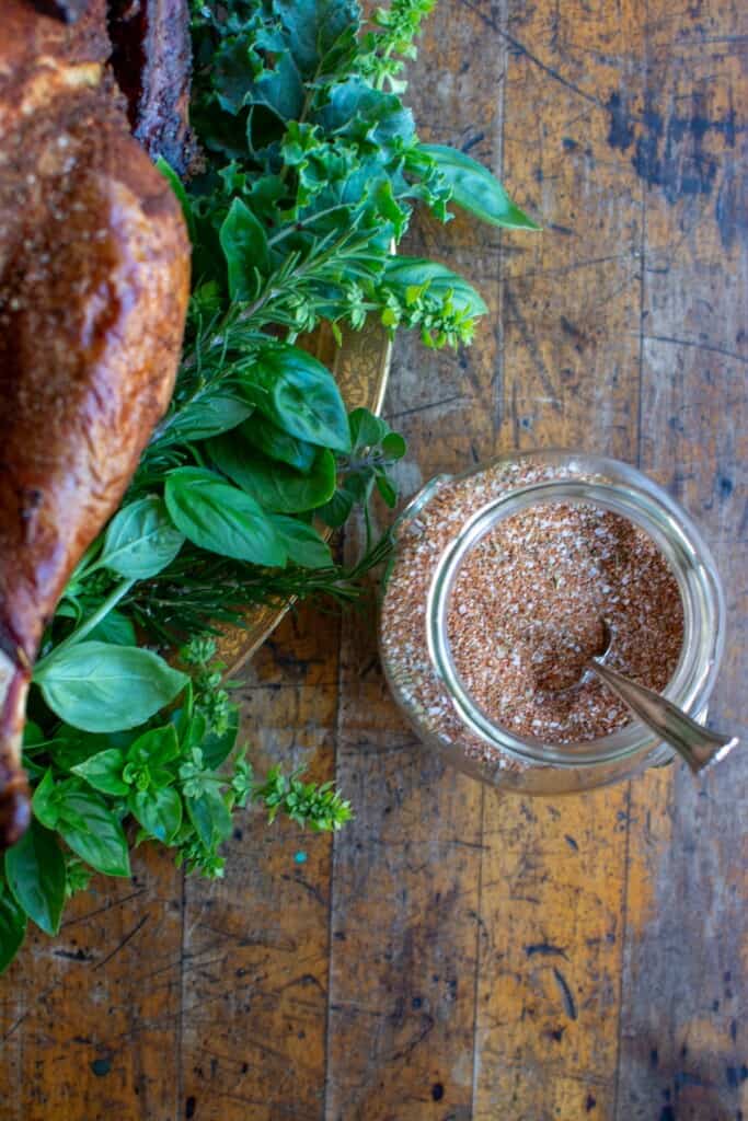 A glass jar of spice rub next to a turkey on a platter