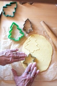 A hand cutting out Christmas cookies with cookie cutters.