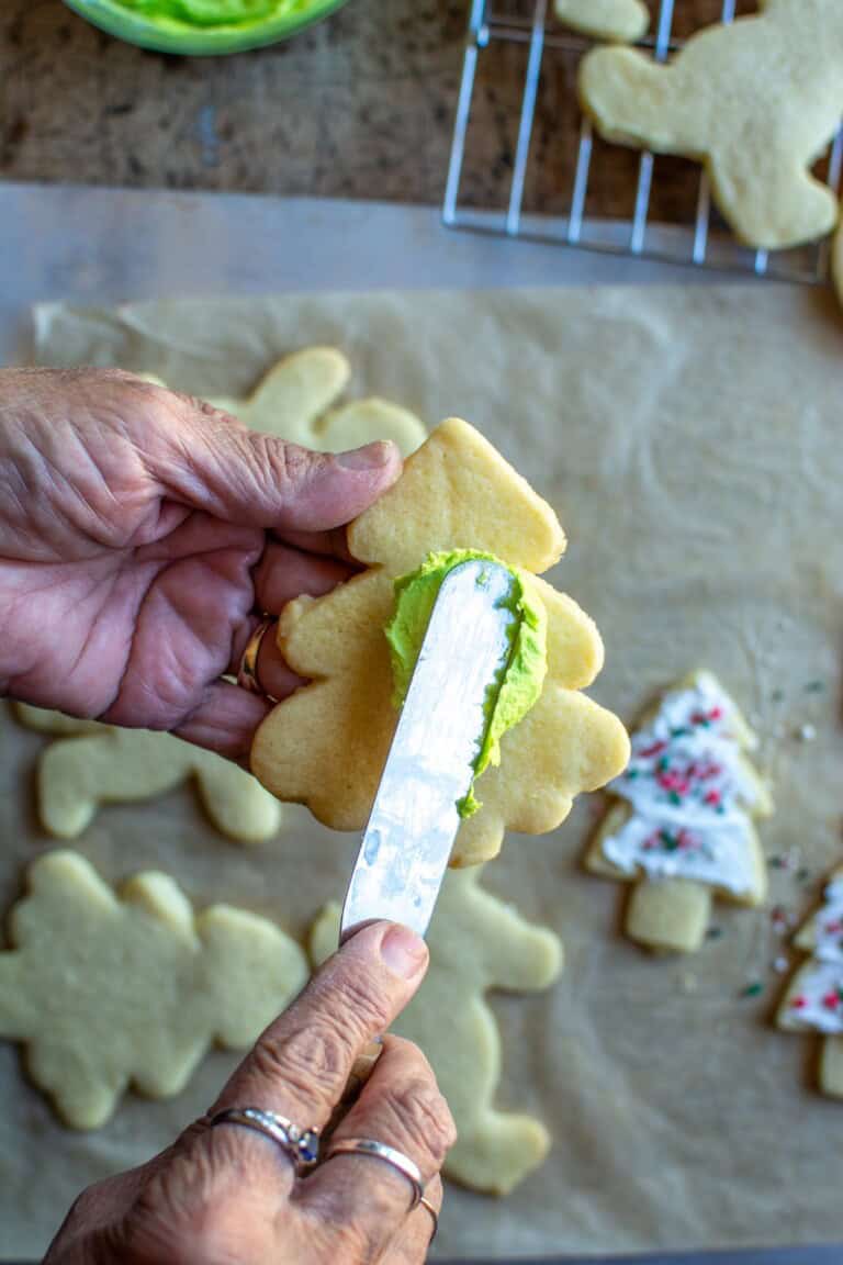 A Christmas tree Christmas Cookie with hands putting icing on it.