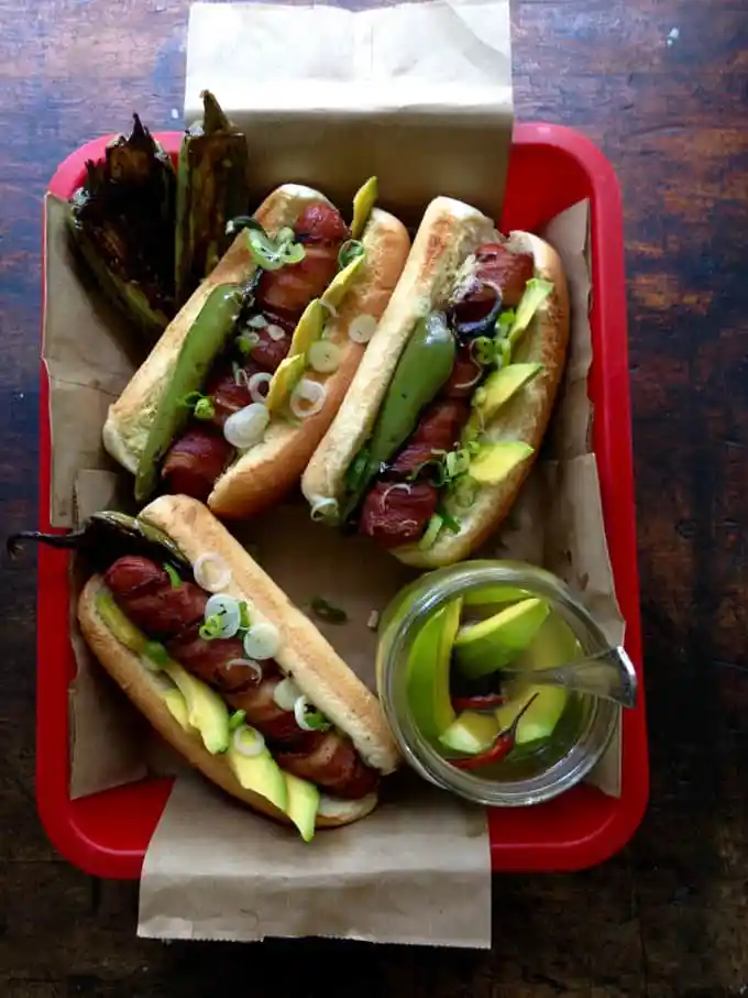 three bacon wrapped hot dogs on a red tray