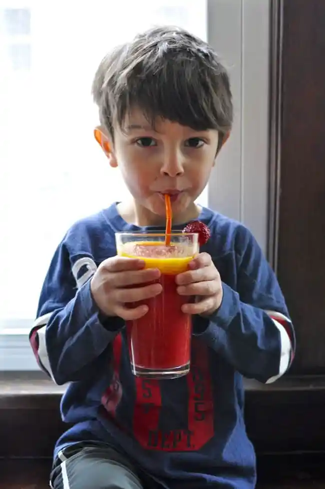 A boy holding a large red smoothie.