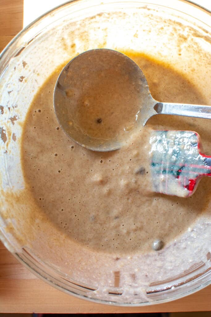 The waffle batter with a ladle and a spatula in the bowl. 