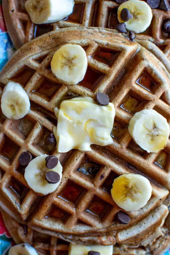 A chocolate chip waffle on a plate with butter on top. 