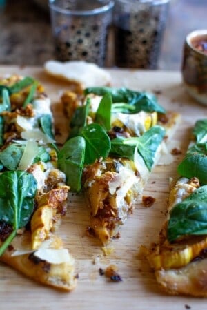 A piece of delicata squash pizza with spinach on top.