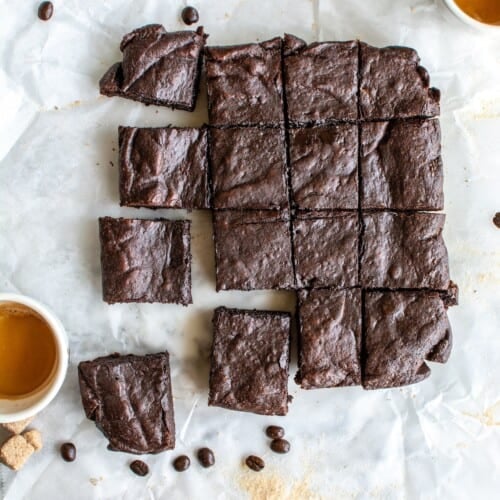 Espresso brownies on a piece of parchment paper with cups of espresso next to them.