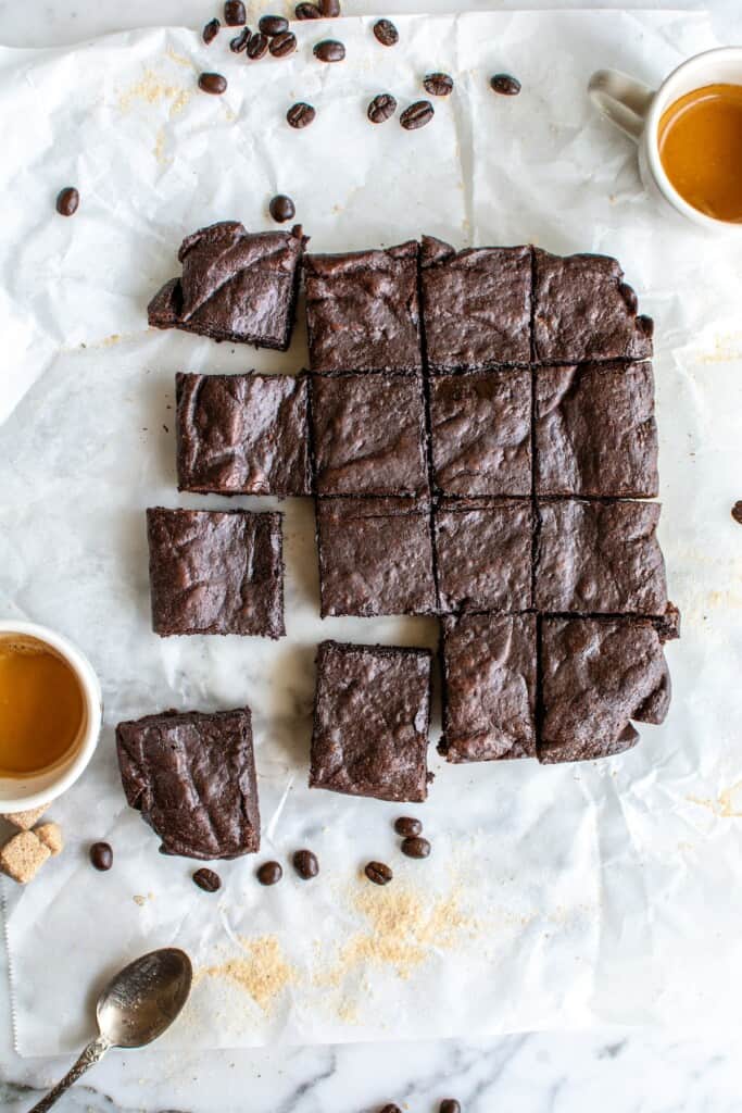 Espresso brownies on a piece of parchment paper with cups of espresso next to them.