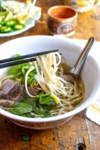 A bowl of beef pho with chopsticks pulling noodles out