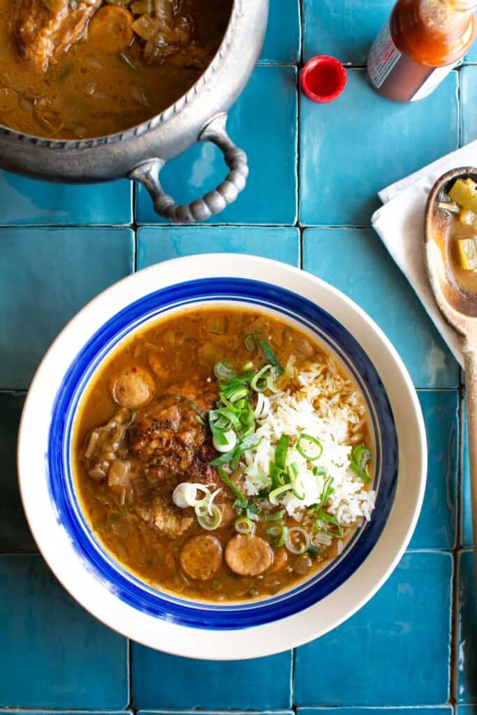 A bowl of gumbo next to a pot full of gumbo