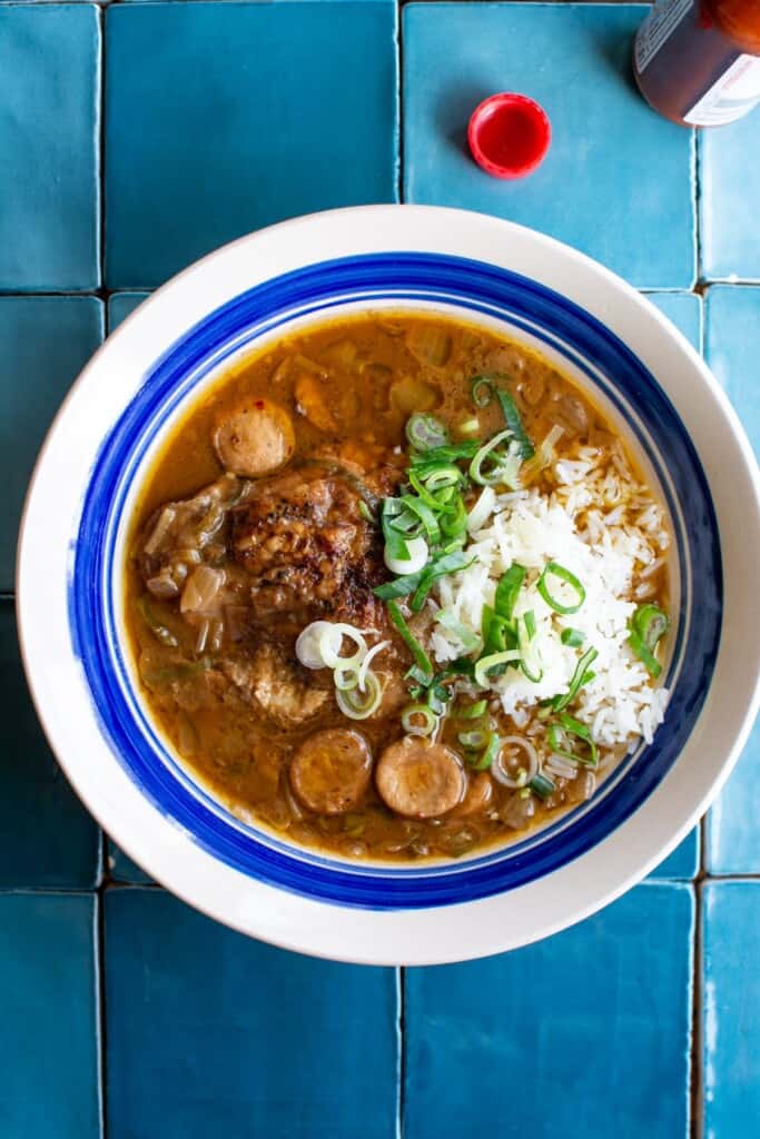 a bowl of chicken and smoked sausage gumbo with a scoop of rice on top. 