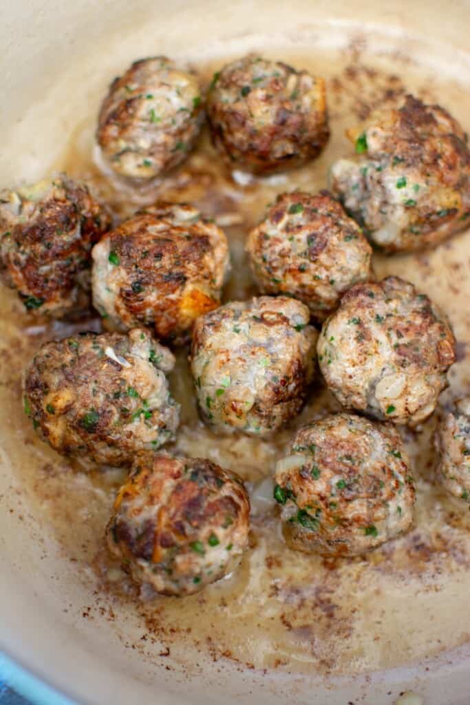 Several meatballs browning in the pot. 