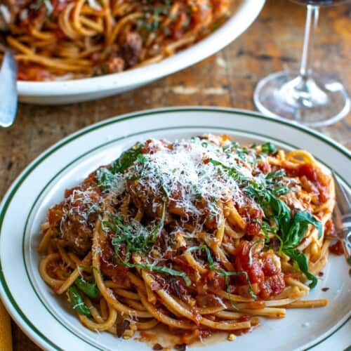 A plate of spaghetti and meatballs with a glass of wine in the back.