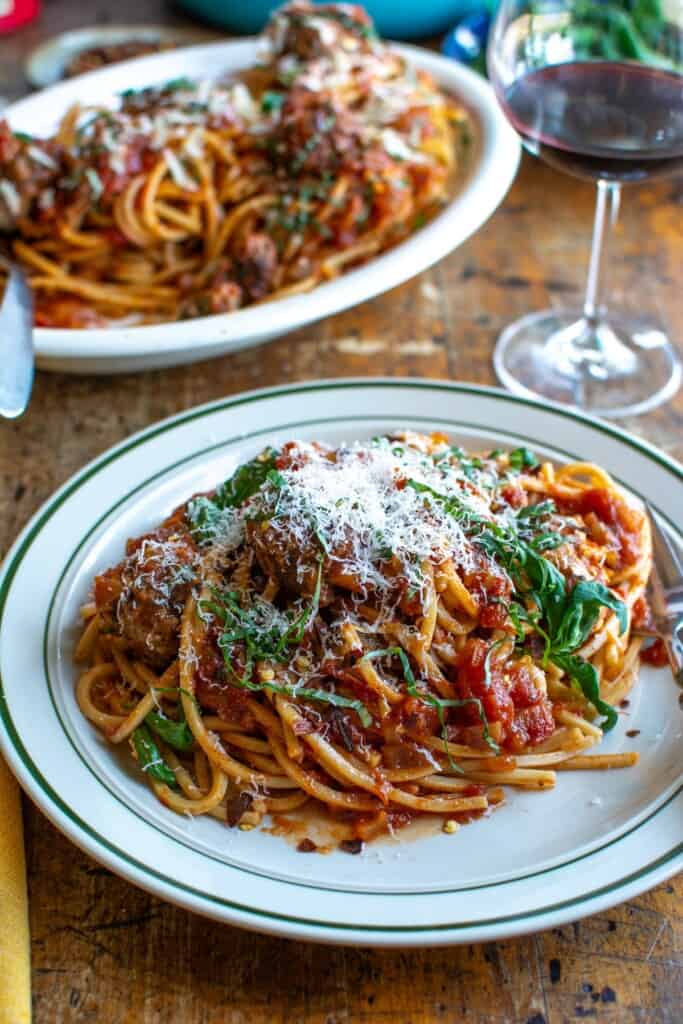 A plate of spaghetti and meatballs with a glass of wine in the back. 