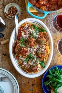 A platter of spaghetti and meatballs with a pot of meatballs next to it.