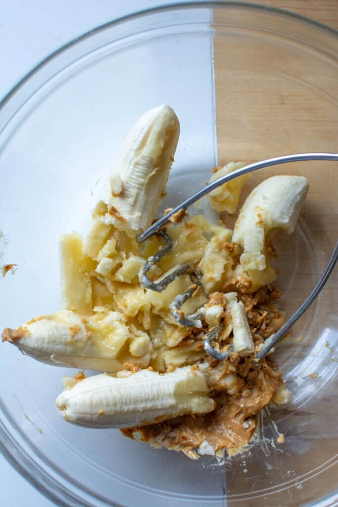 Bananas and peanut butter being mashed in a bowl