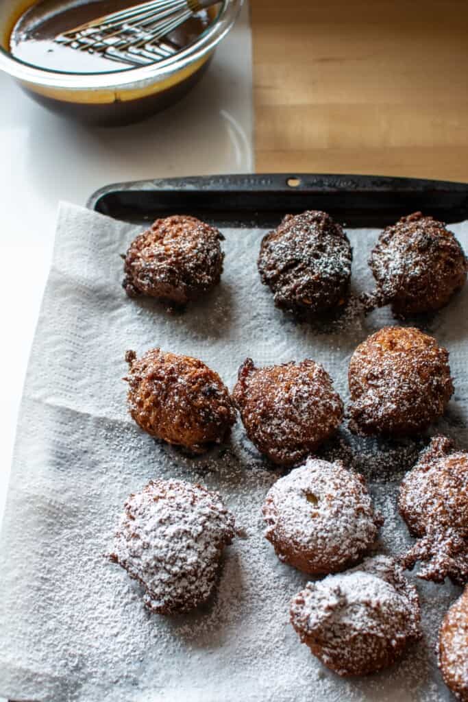 fritters with powdered sugar on then on a paper towel-lined baking sheet
