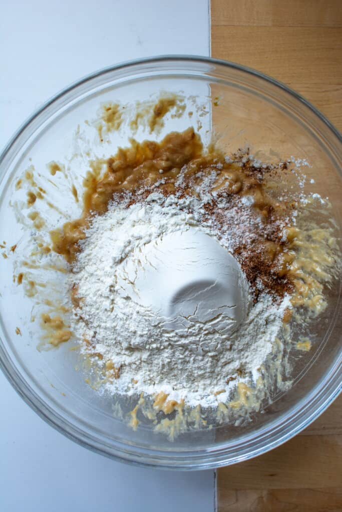 flour and spices on top of mashed bananas in a glass bowl