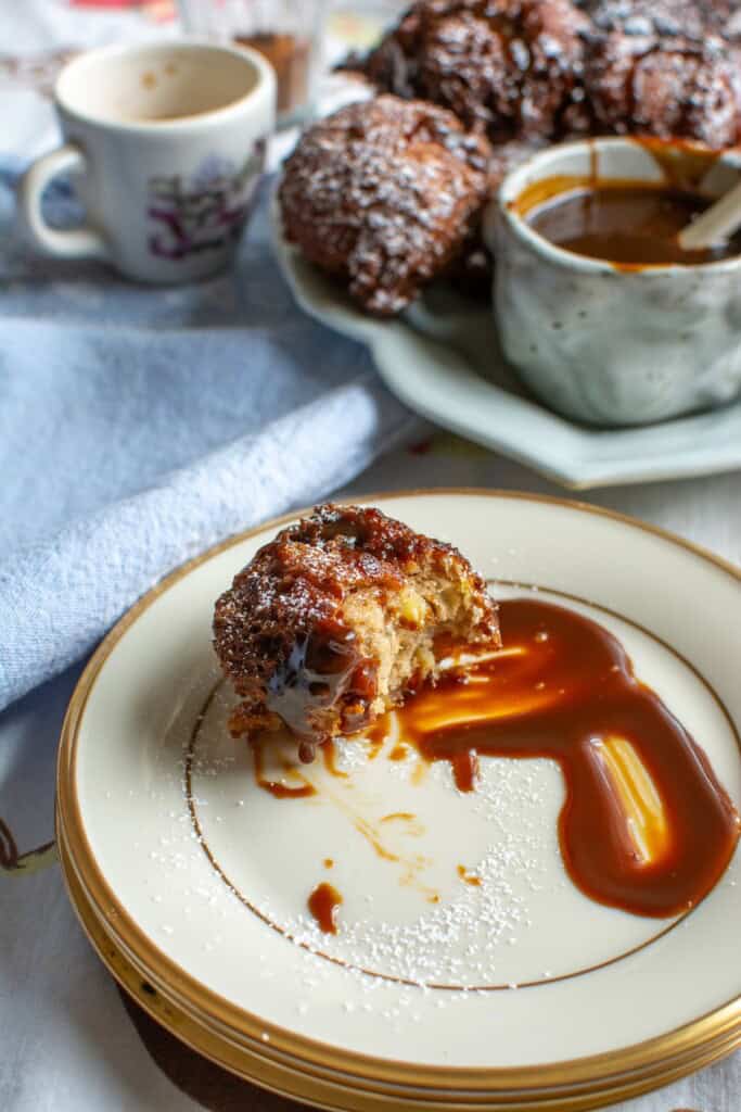 A fritter on a plate with caramel sauce with a bite taken out of it