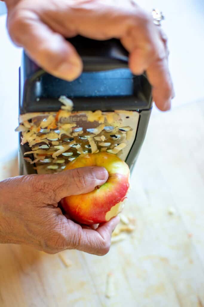 An apple being grated on a box grater.