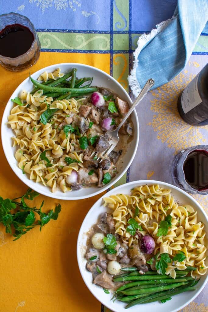 Two plates of chicken fricassee with noodles and green beans