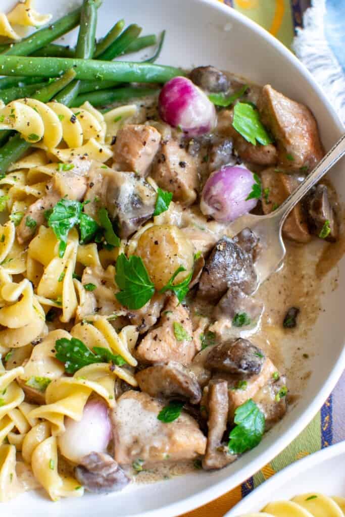 A plate of chicken fricassee with noodles and green beans